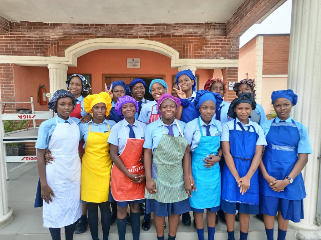 Pedrisi girls in aprons and chef hats posing outside the school